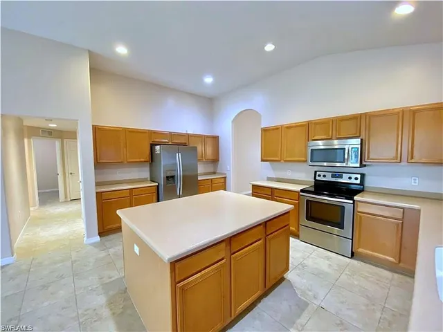 Kitchen featuring a central island with solid-surface countertops, wood cabinetry, recessed ceiling lighting, and stainless-steel appliances