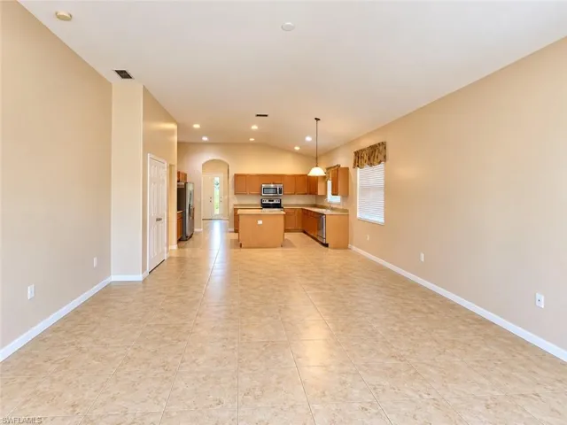 Open-concept interior featuring large-format tile flooring, recessed ceiling lighting, a central kitchen island, wood-finish cabinetry, and vaulted ceilings