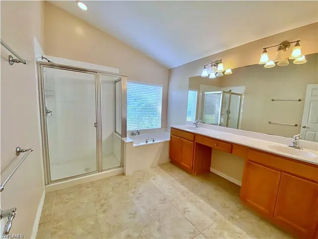Bathroom featuring a glass-enclosed shower, soaking tub, dual-sink vanity with wood cabinetry, and large wall-mounted mirror