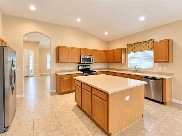 Kitchen featuring natural wood cabinetry, central island with a solid-surface countertop, stainless steel appliances, recessed ceiling lighting, and ceramic tile flooring