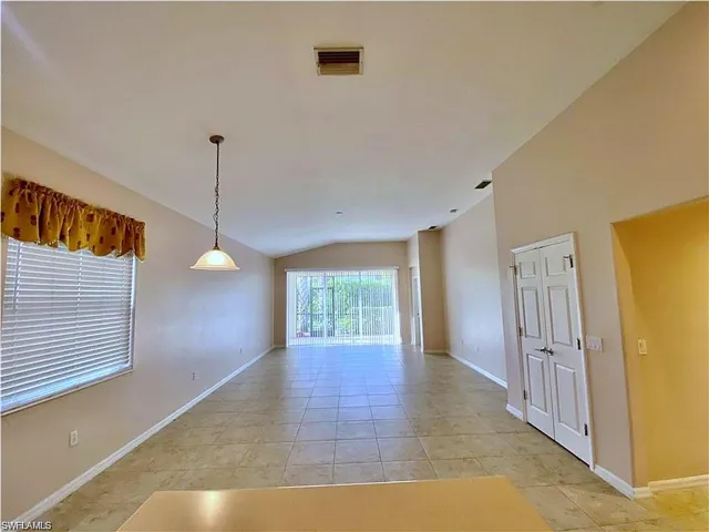 Vaulted ceilings, large-format tile flooring, single-pendant lighting, and sliding glass doors with exterior screen enclosure