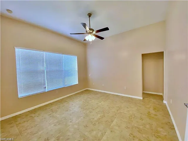 Vaulted ceiling featuring a central multi-blade ceiling fan with integrated light fixture, large-format tile flooring, and oversized window with horizontal blinds