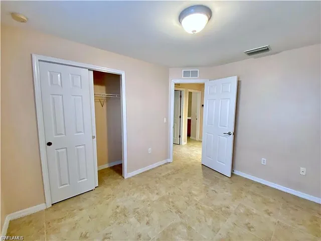 Neutral-toned interior space featuring light-colored tile flooring, two white paneled doors, a walk-in closet with built-in shelving, and a flush-mount ceiling light fixture