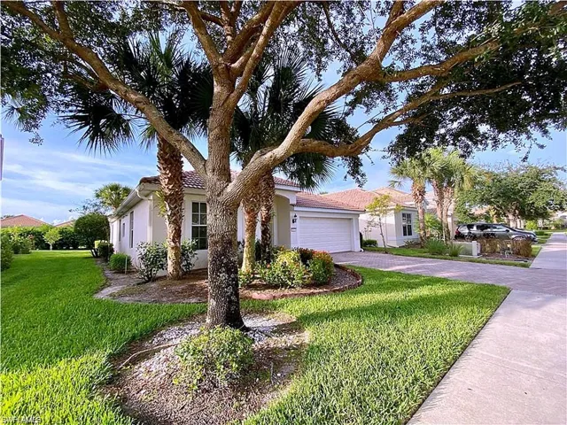 Stucco exterior featuring a paved driveway, tile roof, mature landscaping, and palm trees