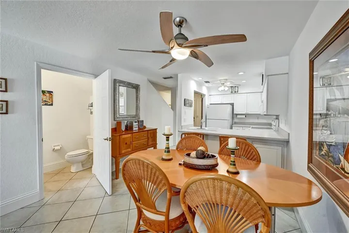 Open-concept dining area featuring a ceiling fan, tile flooring, and a pass-through kitchen with white cabinetry and built-in appliances
