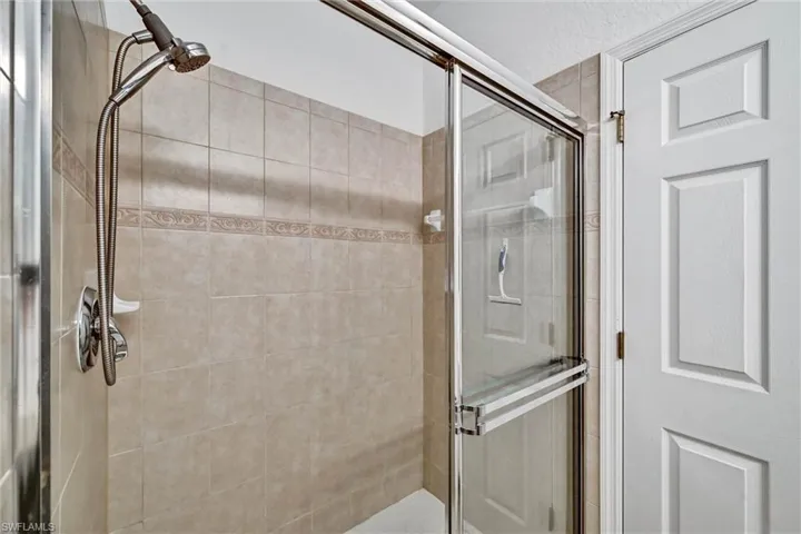Shower enclosure featuring glass sliding doors, a hand-held shower fixture, and tiled walls with decorative banding