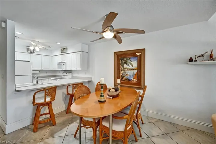 Open-concept living space featuring a kitchen with white cabinetry and a breakfast bar, complemented by a dining area with tile flooring and a ceiling fan