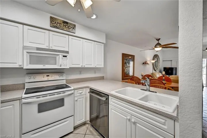 Kitchen featuring white cabinetry, light-toned countertops, a built-in microwave, a white electric range, and a double basin sink with a chrome faucet