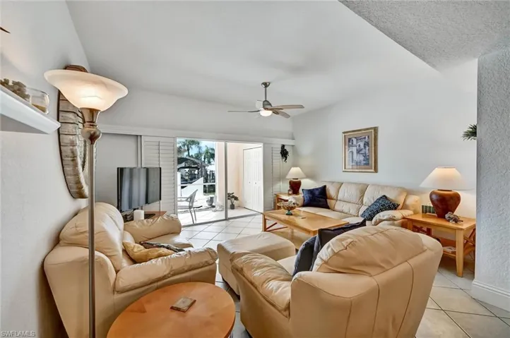 Spacious living area featuring tiled flooring, a ceiling fan, and sliding glass doors with vertical blinds that open to a patio
