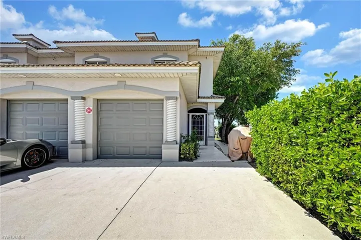 Exterior facade featuring two garage doors, an arched entryway, and a mature hedge