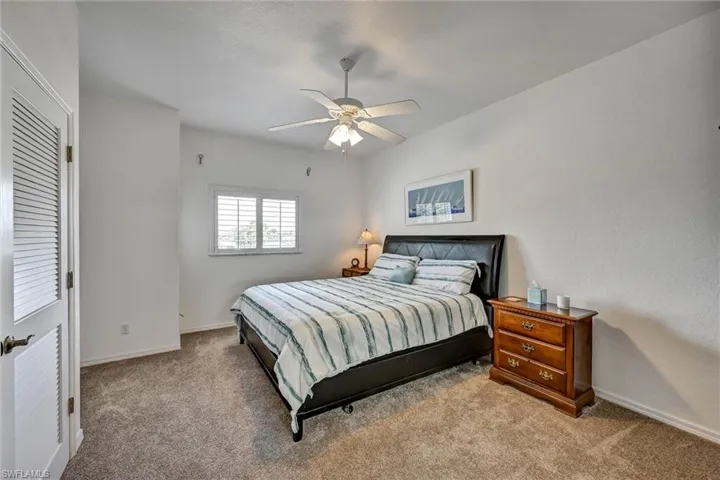 Carpeted room featuring a ceiling fan with integrated lighting, a window with plantation shutters, and a louvered bi-fold door