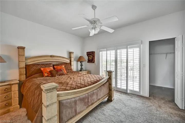 Bedroom featuring plush carpeting, a ceiling fan with light fixture, sliding glass doors with plantation shutters, and a closet with bifold doors and built-in shelving