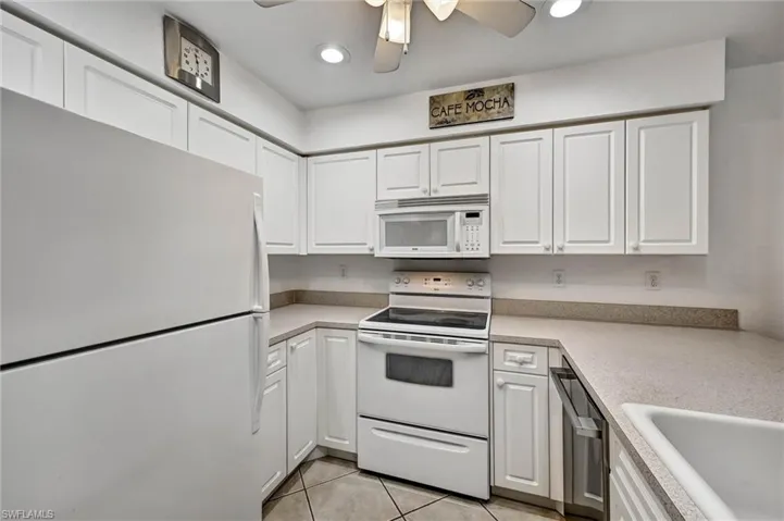Kitchen featuring white cabinetry, white appliances, speckled countertops, and ceiling fan with integrated lighting