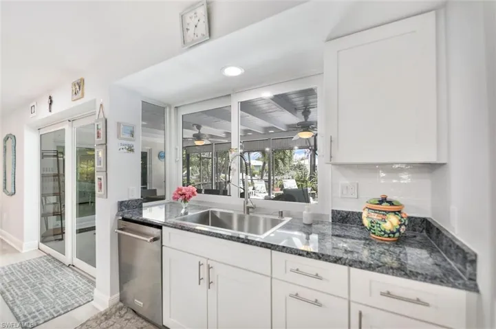 Kitchen featuring white cabinetry, stainless steel dishwasher, recessed lighting, dark stone countertops, and a sunroom