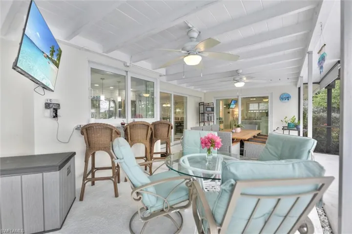 Sunroom featuring outdoor dining space, beam ceiling, a patio area, and ceiling fan