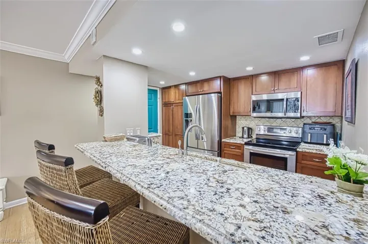 Kitchen featuring stainless steel appliances, a breakfast bar, decorative backsplash, brown cabinetry, and light stone countertops