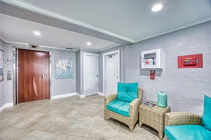Living area with a textured wall, elevator, ornamental molding, tile patterned floors, and recessed lighting