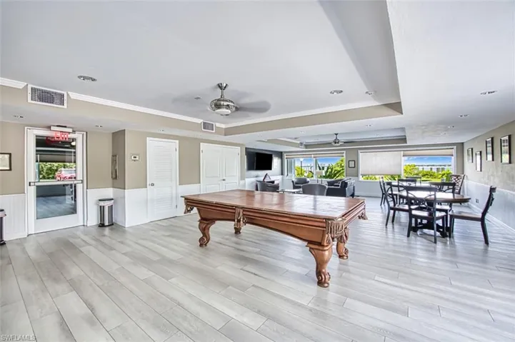 Recreation room with ceiling fan, a tray ceiling, billiards, wainscoting, and light wood-type flooring