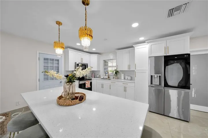 Kitchen with decorative light fixtures, appliances with stainless steel finishes, a chandelier, white cabinetry, and sink