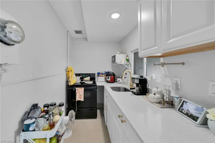 Kitchen featuring black electric range oven, sink, and white cabinets