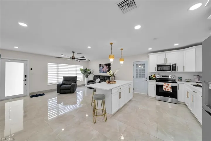 Kitchen featuring a kitchen island, a kitchen breakfast bar, stainless steel appliances, ceiling fan, and white cabinets