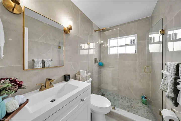 Bathroom with a shower with shower door, toilet, vanity, and tile walls