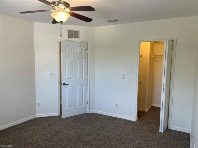 Unfurnished bedroom with dark colored carpet, a spacious closet, and a ceiling fan