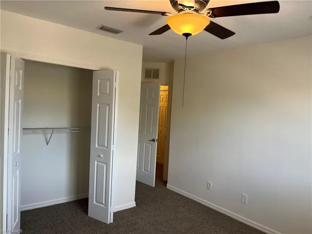 Unfurnished bedroom with dark colored carpet, a closet, and ceiling fan