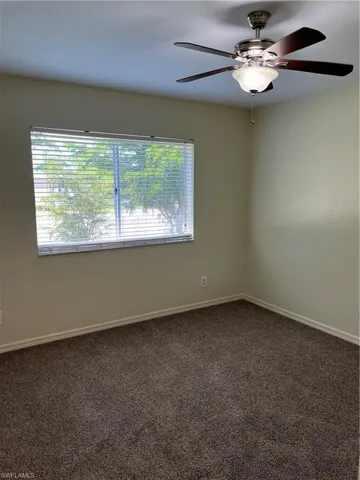 Unfurnished room featuring dark carpet and a ceiling fan