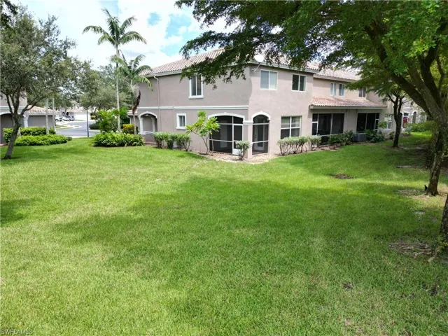 Rear view of property featuring a tiled roof, stucco siding, a lawn, and a sunroom