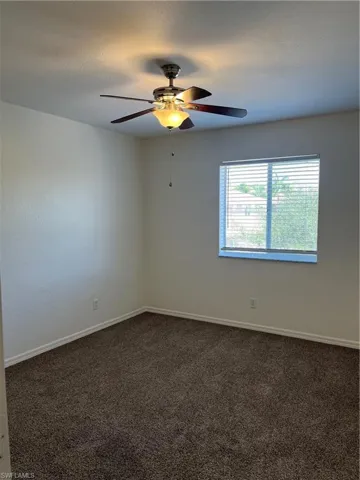 Spare room featuring dark carpet, a textured ceiling, and a ceiling fan