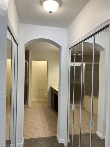 Hall featuring light tile patterned floors, arched walkways, a textured wall, and a textured ceiling