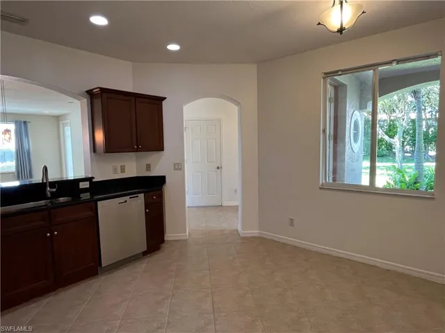 Kitchen with dark brown cabinetry, white dishwasher, arched walkways, recessed lighting, and light tile patterned floors