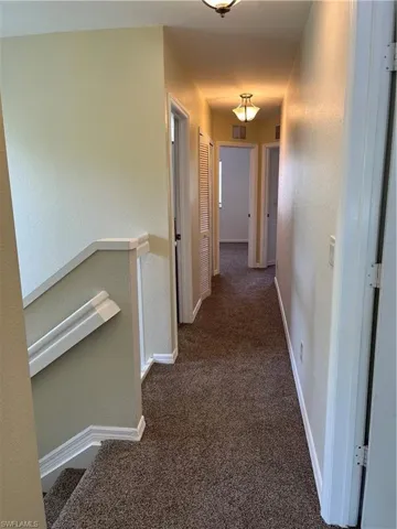 Hallway with a textured wall, dark carpet, and an upstairs landing