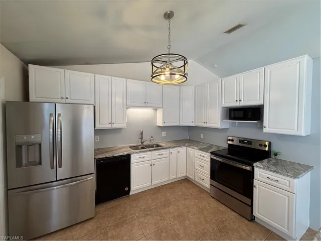 Kitchen featuring paneled fridge, stove, lofted ceiling, white cabinetry, and decorative light fixtures