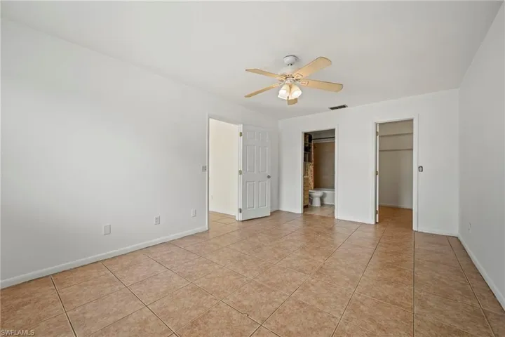 Unfurnished bedroom with a walk in closet, light tile patterned flooring, ceiling fan, and ensuite bathroom