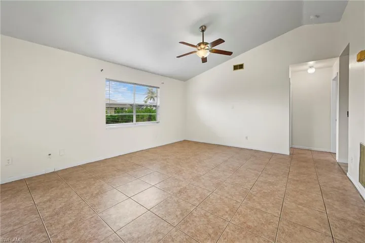 Empty room featuring lofted ceiling, a ceiling fan, and light tile patterned floors