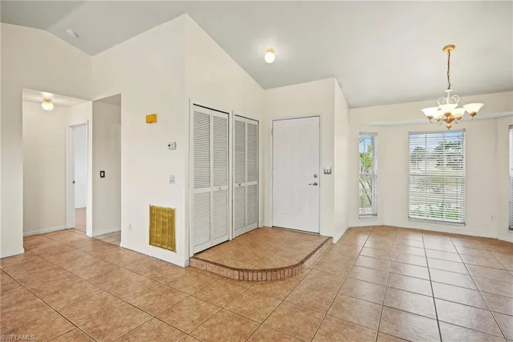 Foyer entrance featuring vaulted ceiling, light tile patterned floors, and a chandelier
