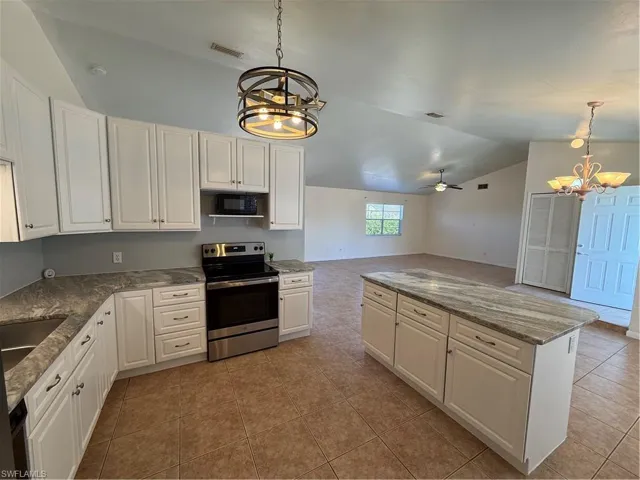 Kitchen featuring hanging lights, range, open floor plan, white cabinetry, and lofted ceiling