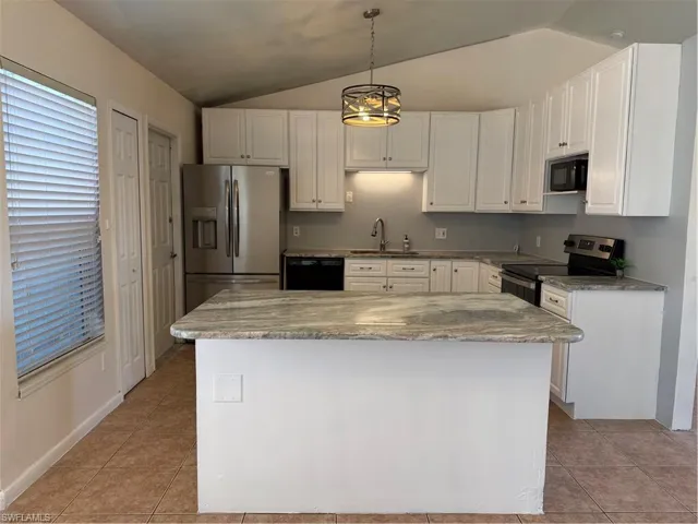 Kitchen featuring white cabinets, stove, lofted ceiling, a kitchen island, and light tile patterned floors
