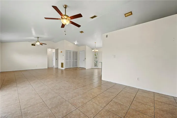 Empty room featuring lofted ceiling, a ceiling fan, a chandelier, and light tile patterned flooring