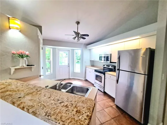 Kitchen with appliances with stainless steel finishes, light tile patterned floors, a ceiling fan, and a peninsula