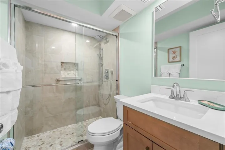 Bathroom featuring a vanity with white stone-finish countertop, shower enclosure with glass doors and tile surround, recessed wall niche, pebble-texture shower floor, and large rectangular mirror