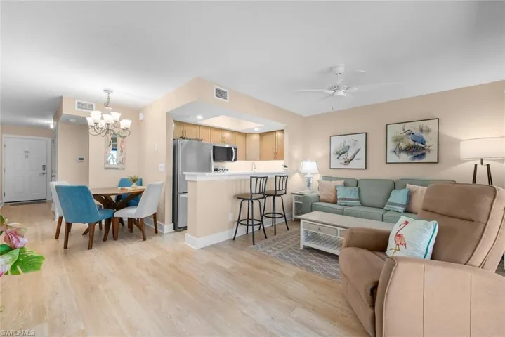Open-concept interior featuring wood-finish flooring, a kitchen breakfast bar, stainless steel refrigerator, and a recessed ceiling lighting fixture