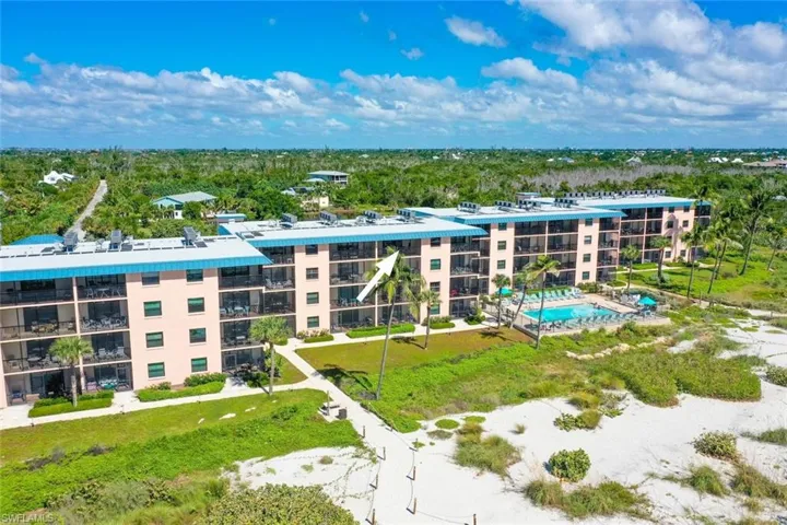 Multi-story complex featuring private balconies, building-integrated solar panels, and a ground-level swimming pool with paved sun deck, set against sandy coastal grounds with native vegetation