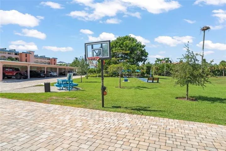Expansive grounds featuring a paver driveway, basketball hoop, covered parking area, and manicured green space with mature trees