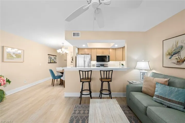 Kitchen featuring light wood-finish cabinetry, stainless steel appliances, and a breakfast bar, complemented by wood-finish flooring and a ceiling fan