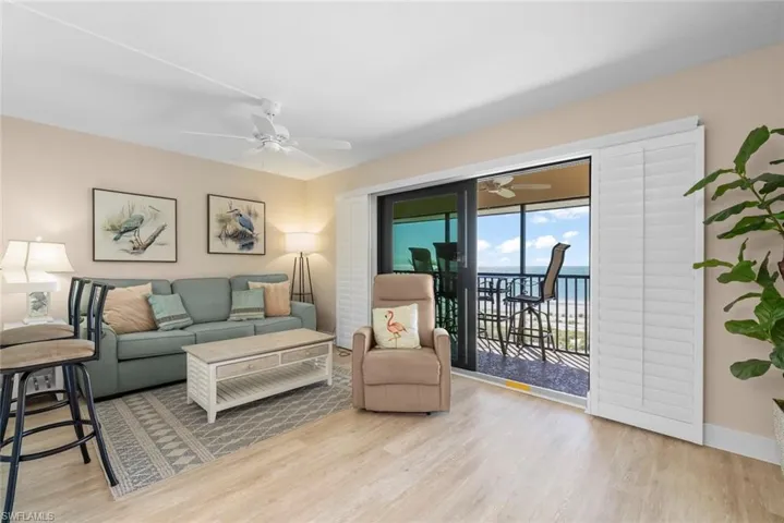 Living area featuring wood-finish flooring, a ceiling fan, and large sliding glass doors with white plantation shutters opening to a covered balcony