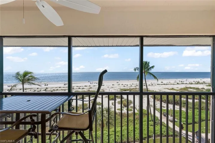 Screened lanai featuring a ceiling fan and metal railing overlooking the coastline, sandy beach, and ocean