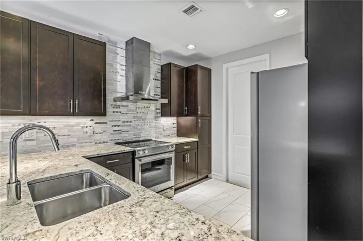 Kitchen with stainless steel appliances, dark wood finish cabinets, light stone countertops, light marble finish floors, and tasteful backsplash